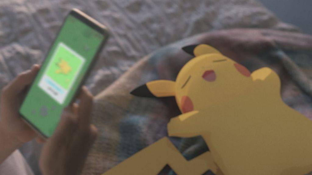 Un pikachu somnolent, avec une personne tenant un téléphone en utilisant l'application Pokemon Sleep